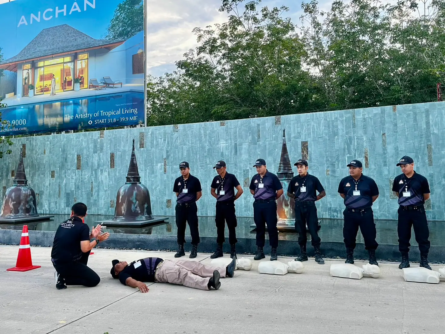 SGS instructor kneeling beside an unresponsive casualty demonstrating the response check while officers observe at Anchan, Thalang