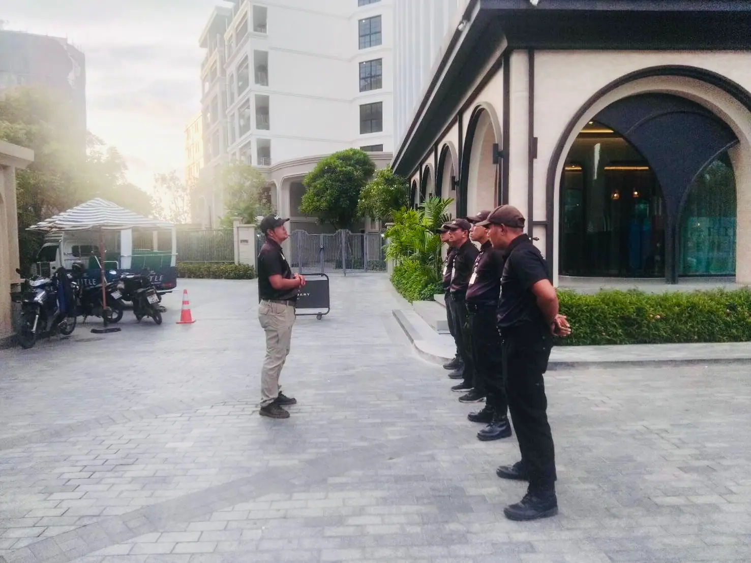 SGS supervisor addressing four security officers lined up along the entrance arcade at The Title Legendary, Bangtao, in low sunlight