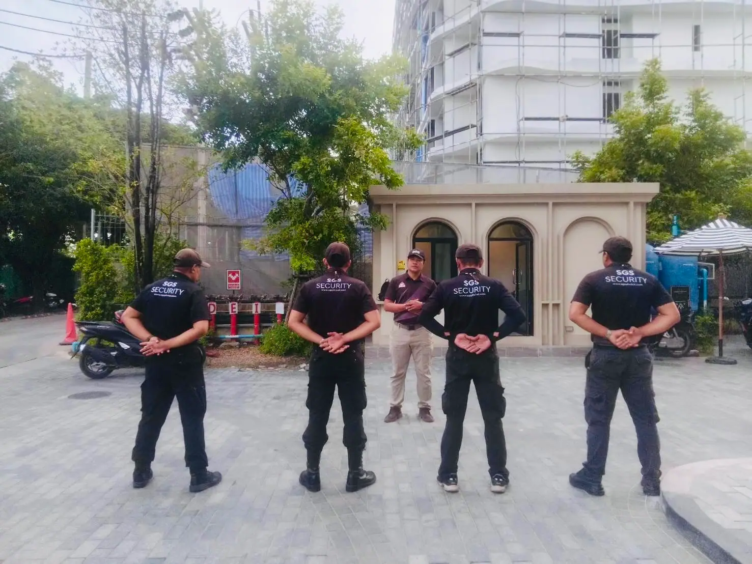 Four SGS security officers standing at ease facing a supervisor outside the gatehouse at The Title Legendary, Bangtao, with construction scaffolding behind